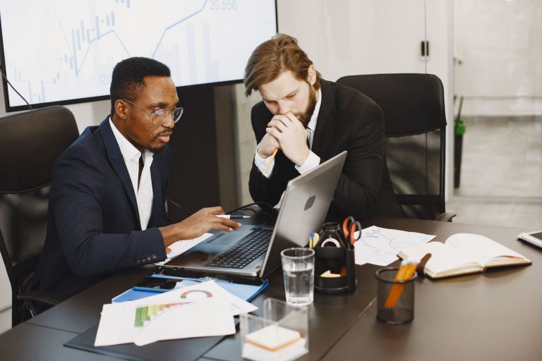 Two businessmen engaged in a strategy meeting with laptops and charts. — How Pak Game Combines Skill, Strategy, and Quick Thi